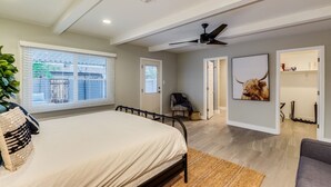 Ein Schlafzimmer mit einem Bett, einem Deckenventilator, einem Fenster mit Jalousien und einer Tür zu einem anderen Raum.