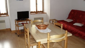 A dining area with a table, chairs, a television, and a red sofa. - Mountain apartment 6 people (Génos)