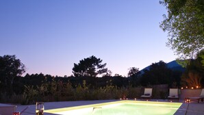 Zona de piscina al aire libre con una mesa para dos, con una copa de vino, una vela y un cuenco de fruta.