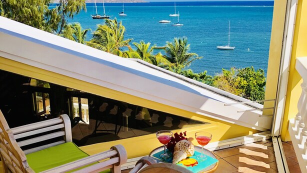 Varanda com vista para o mar, cadeiras de madeira, uma mesa com bebidas e uma concha decorativa.