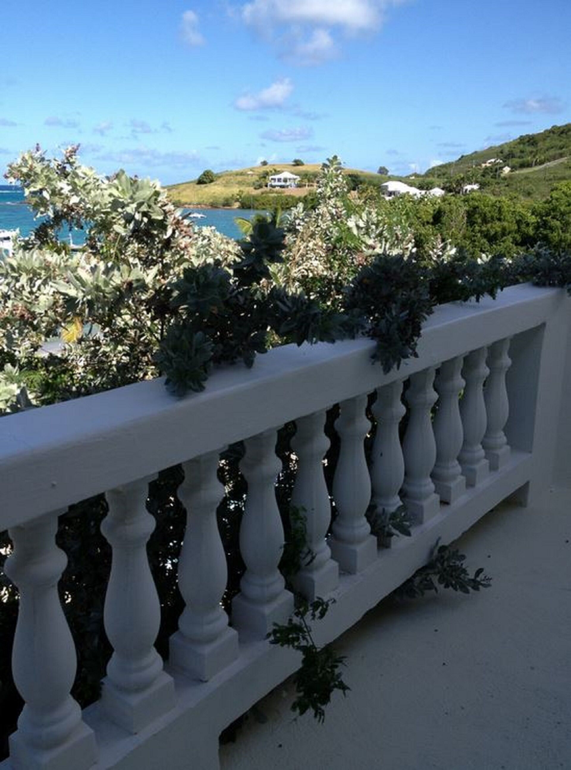 Ein Balkon mit weißer Brüstung, der auf eine Küstenlandschaft mit einem Haus in der Ferne blickt.