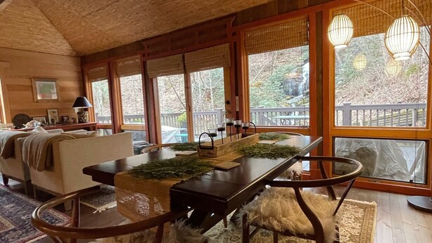 Ein gemütliches Blockhaus-Interieur mit einem Holzesstisch, Stühlen und einem großen Fenster mit Blick ins Freie.