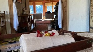 Ein Zimmer mit einem Bett, einer Holzbank, einem kleinen Tisch und einem Stuhl. Ein Fenster bietet Blick ins Freie.