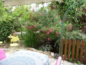 Une terrasse de jardin agrémentée d’un petit bassin, entourée d’une végétation luxuriante et de fleurs roses.