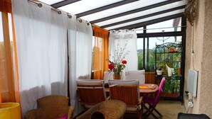 Een overdekt terras met rieten meubilair, een tafel en een barbecue.
