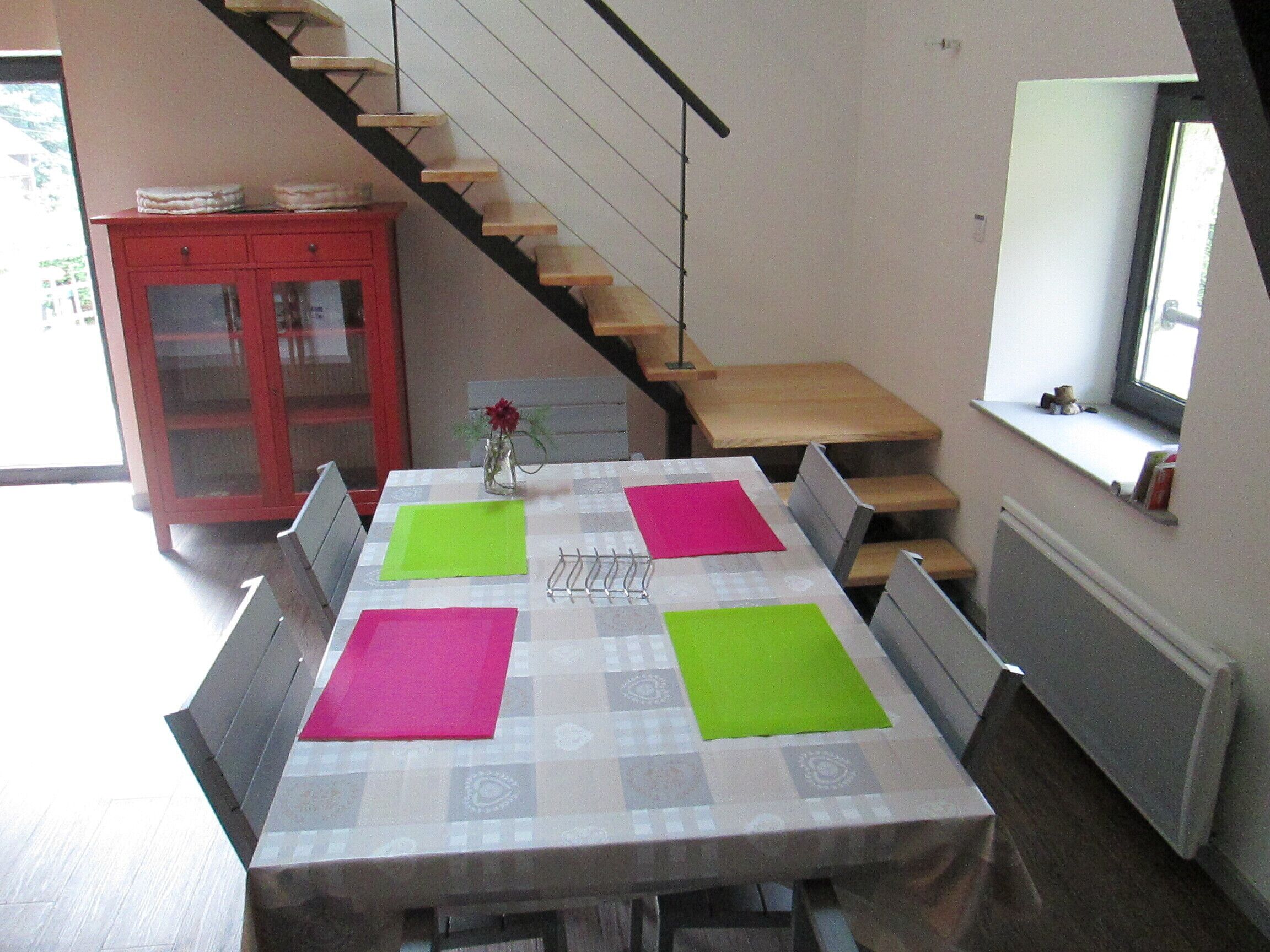 A dining area with a table set for four, a red cabinet, and a staircase.