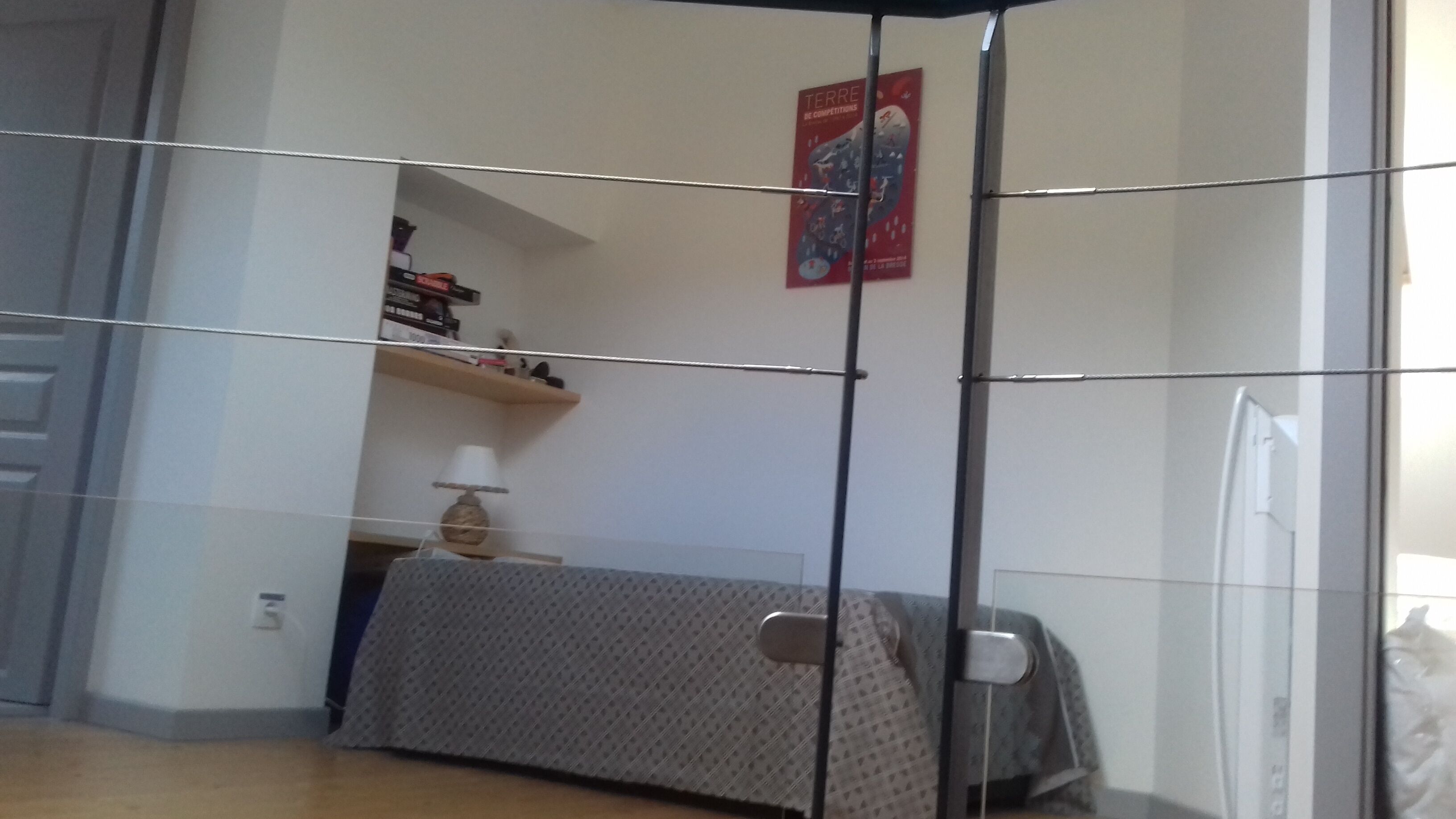 A room with a bed, a shelf with books, a lamp, and a poster on the wall.