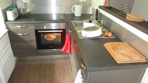 A compact kitchen with a built-in oven, a sink, and a wooden cutting board on the countertop. - Duplex "La Ferme de Paul" 6 Pers. + baby - Altitude 800 m'at 2 km Ski slopes (La Bresse)