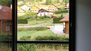 A room with a large window overlooking a residential area with houses and a well-maintained lawn. - Duplex "La Ferme de Paul" 6 Pers. + baby - Altitude 800 m'at 2 km Ski slopes (La Bresse)