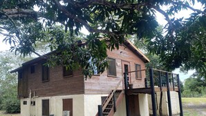 A two-story wooden house with a balcony and a staircase leading to the upper floor.