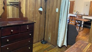 A wooden interior with a dresser, a floor lamp, a table, and a kitchen area with a stove.