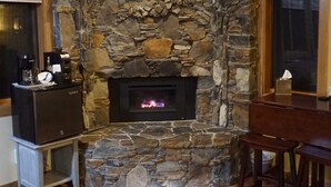 Una chimenea de piedra con fuego, suelo de madera, una zona de café y un comedor.