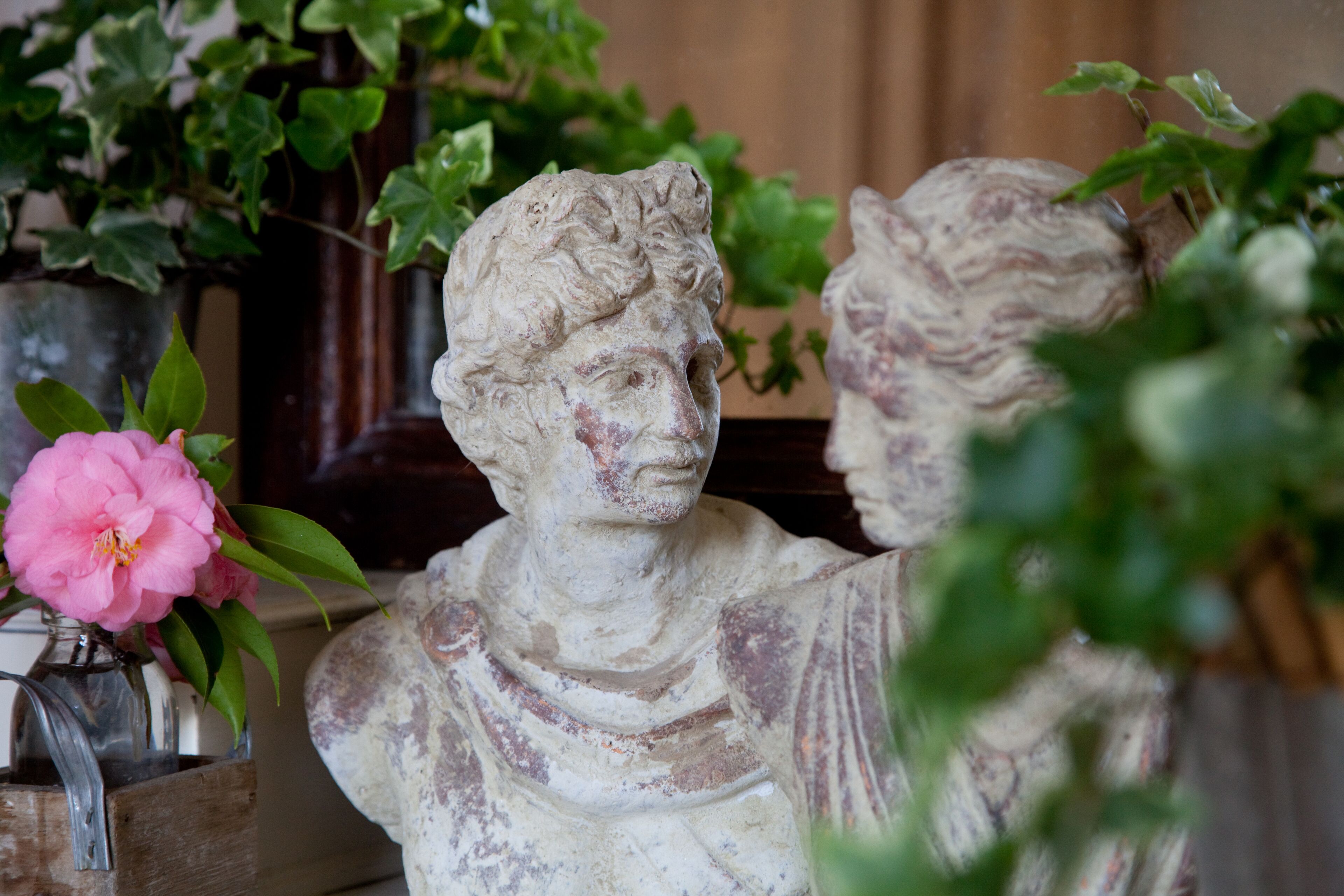 A marble bust sculpture in a room with a wooden cabinet and a potted plant with pink flowers.