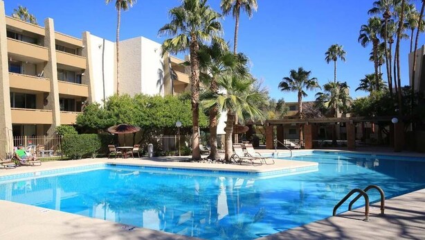 A swimming pool with palm trees and lounge chairs, surrounded by a building with multiple balconies. - Old Town Scottsdale Getaway - Spectacular Pool View (Scottsdale)