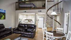 A spacious living area with a leather sofa, a coffee table, and a dining table with chairs. A staircase leads to an upper level. - 🌄Resort Vacations at Fairfield Glade TN  Completely remodeled golf villa! (Fairfield Glade)