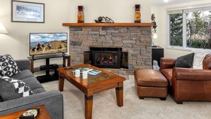 A living room with a stone fireplace, leather furniture, and a television on a stand. - Terracehouse 2BR Ski Getaway, Steps to Lifts, Fireplace + Hot Tub (Snowmass Village)