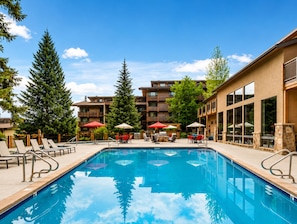 A swimming pool with lounge chairs and umbrellas, surrounded by multi-story buildings with balconies.