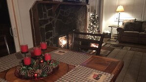 A cozy living room with a fireplace, a Christmas tree, and a dining table set with candles.