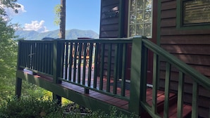 A wooden cabin with a deck, a window, and a mountain view in the background.