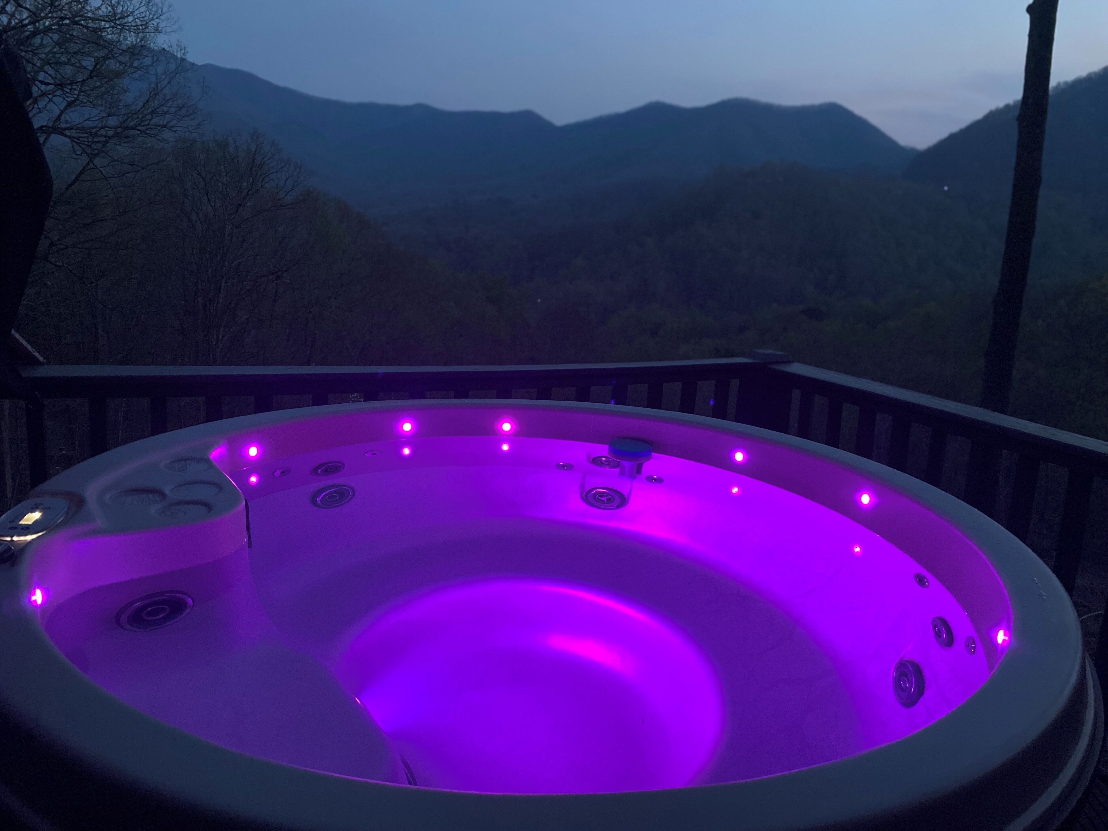 A hot tub with purple lighting, surrounded by a deck with a view of mountains.