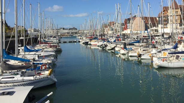 A marina with numerous boats docked along a calm waterway, surrounded by buildings. - Two-room apartment with balcony, indoor heated pool - 4 people (Deauville)