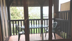 A covered outdoor area with a round table and two chairs, a wooden railing, and a view of greenery outside. - Two-room apartment with balcony, indoor heated pool - 4 people (Deauville)