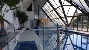 An indoor swimming pool with a glass ceiling, blue pool area, and potted plants. - Two-room apartment with balcony, indoor heated pool - 4 people (Deauville)