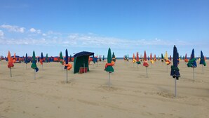 A beach with rows of colorful umbrellas and a small shelter. - Two-room apartment with balcony, indoor heated pool - 4 people (Deauville)