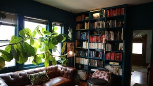 A cozy living room with a leather couch, a small table, a bookshelf filled with books, and a large plant.