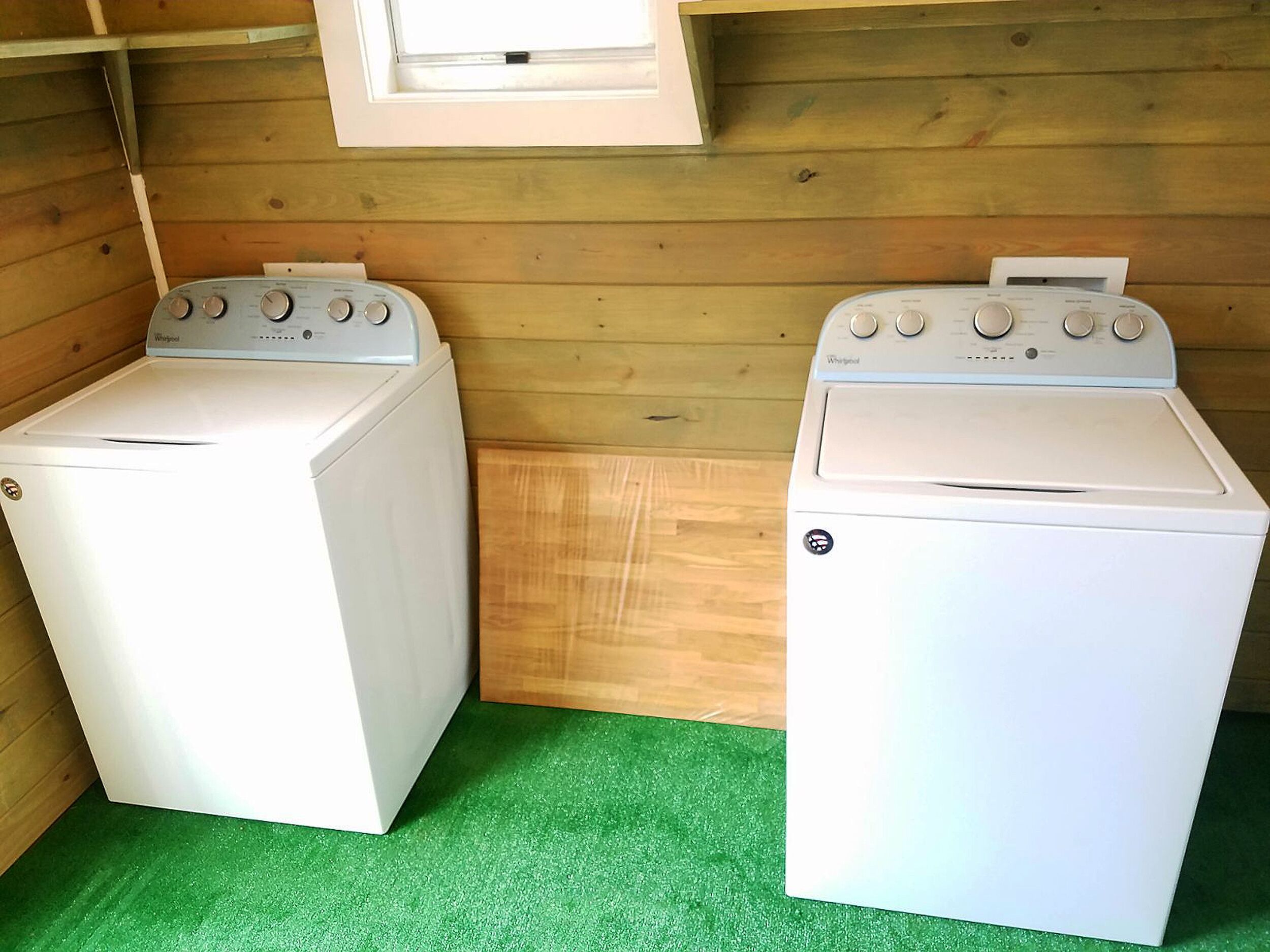 Two white Whirlpool dryers in a small laundry room with wooden walls and a green floor.
