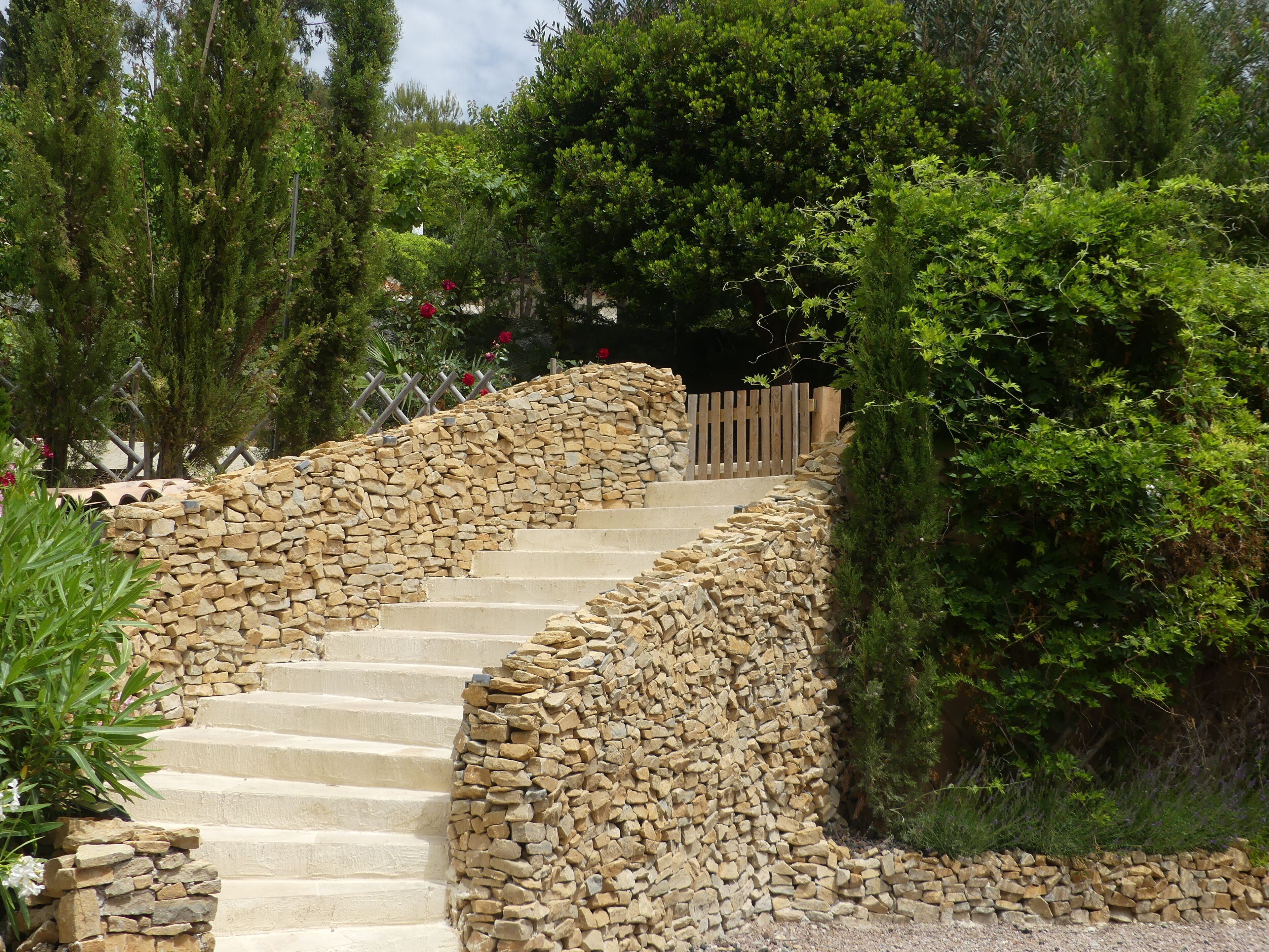 A stone staircase leading up to a wooden gate, surrounded by lush greenery and trees.