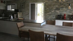 Una cucina moderna con zoccolo in pietra, un'area pranzo con tavolo in marmo e vista sull'esterno tramite una porta in vetro.