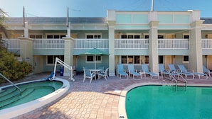 A hotel with a pool area, including lounge chairs and a small table with an umbrella. - Resort Sixty-Six - 1 Bedroom (Holmes Beach)