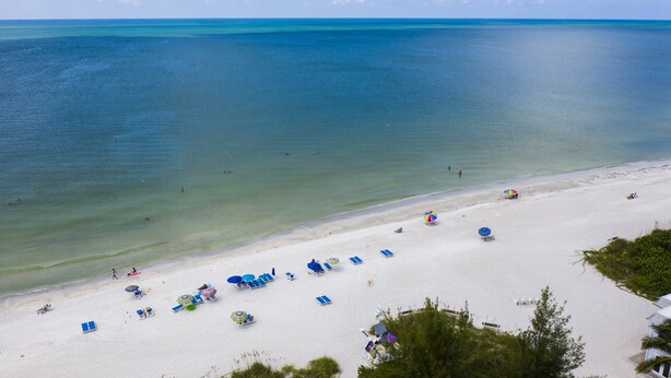 A beach with clear blue water, white sand, and several sun loungers and umbrellas. - Resort Sixty-Six - 1 Bedroom (Holmes Beach)