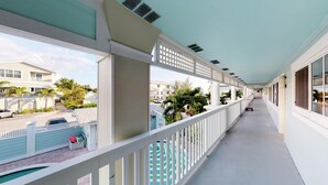 A long corridor with white railings, a view of a street with cars and buildings, and a pool area with a fence and lounge chairs. - Resort Sixty-Six - 1 Bedroom (Holmes Beach)