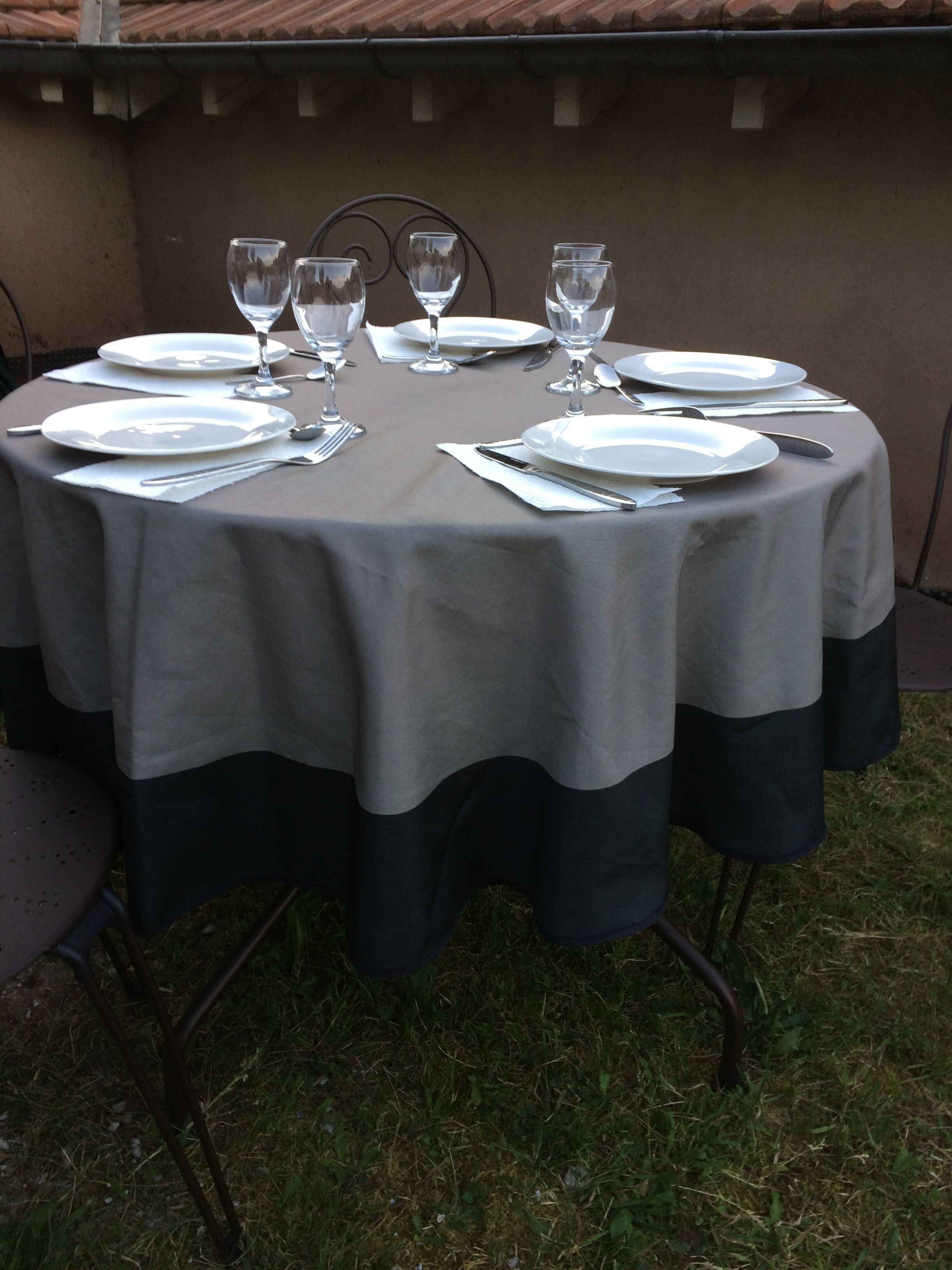 A round table set for dining outdoors with plates, cutlery, and wine glasses.