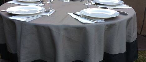 A round table set for dining outdoors with plates, cutlery, and wine glasses.