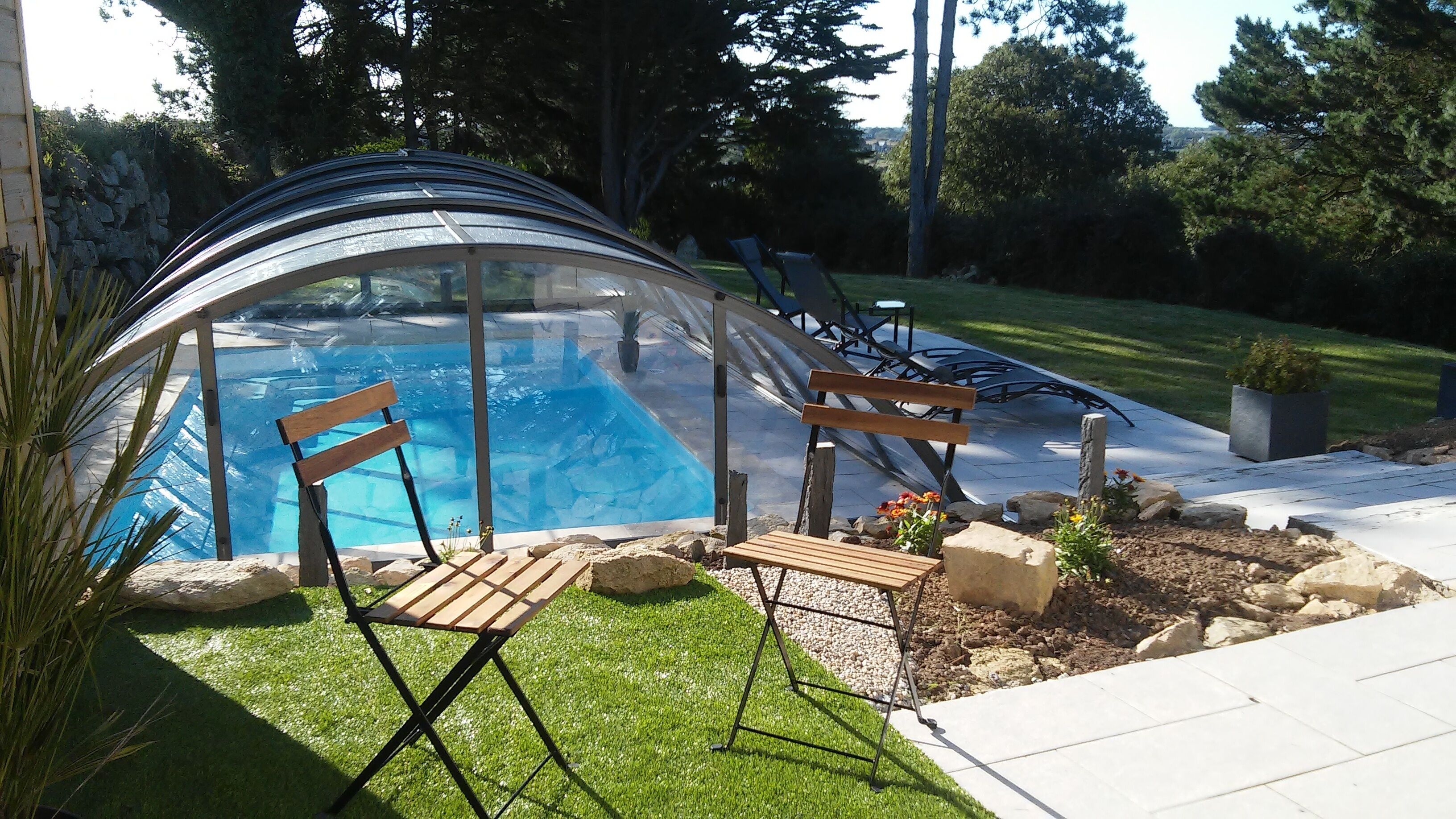 Ein von Glas umgebener Pool mit Holzliegen und einem Steinweg.