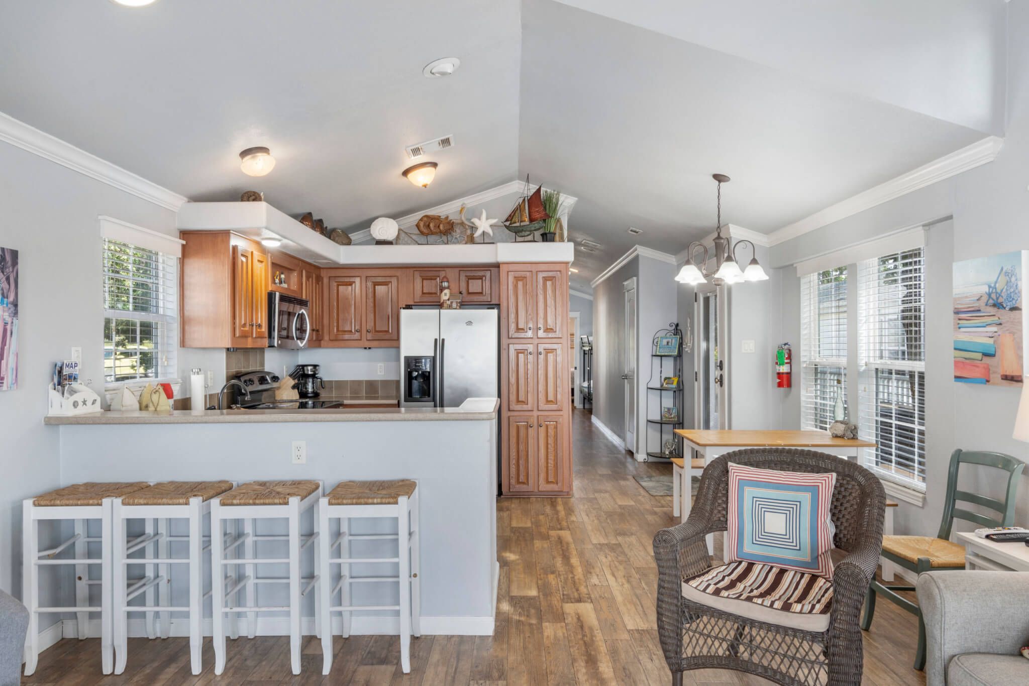 A kitchen with wooden cabinets, a central island with stools, and a dining area with a chair and table.