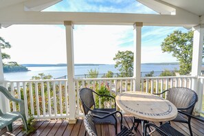 Un espace extérieur abrité, doté d’une terrasse en bois, d’une rambarde blanche et d’une table ronde accompagnée de deux chaises.