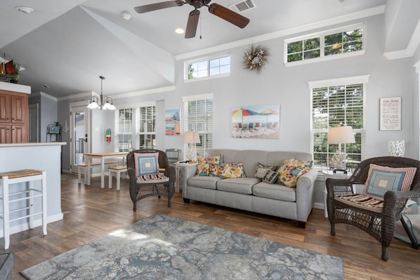 A spacious living area with a grey sofa, wicker chairs, a wooden coffee table, and a large rug.