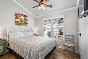 A bedroom with a bed, a ceiling fan, a window with blinds, a chair, and a nightstand with a lamp. - Beachcomber at CrossTimbers Marina (Sperry,)