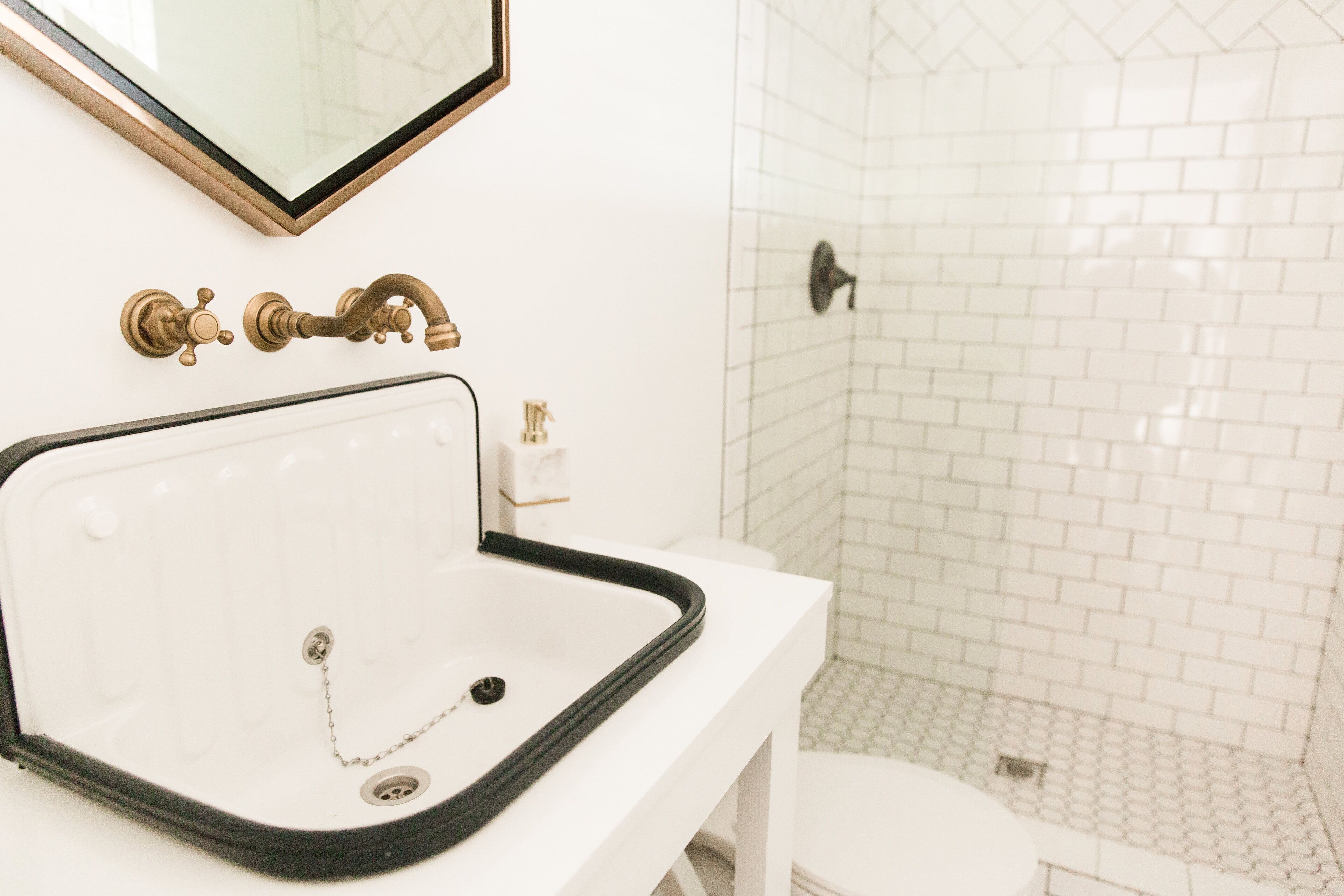 A bathroom with a white sink, a brass faucet, and a tiled shower area.