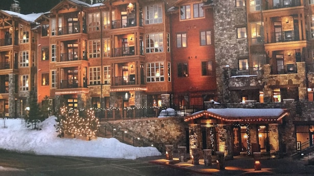 A multi-story hotel with a stone facade, multiple balconies, and a lit entrance. - Surrounded by pine trees and mountains (Truckee)