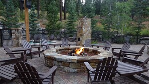An outdoor seating area with a stone fire pit surrounded by Adirondack chairs. - Surrounded by pine trees and mountains (Truckee)