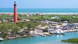 A coastal area with a prominent red lighthouse, a marina with boats, and a parking lot. - Ocean Oasis (Volusia County)