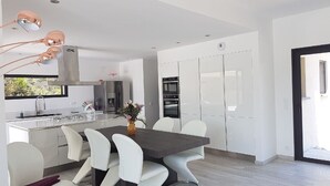 Uma cozinha moderna com armários brancos, uma ilha central e uma área de jantar com cadeiras brancas.