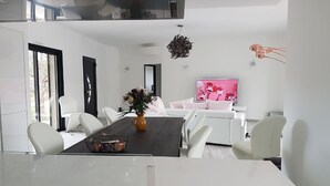 Uma sala de estar moderna com uma mesa de jantar de madeira escura, sofás brancos e uma grande TV de tela plana.