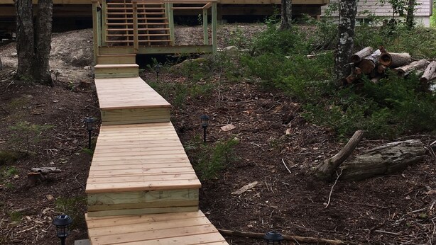 A wooden deck leading to a house with a balcony, surrounded by trees. - Lakefront cottage near Acadia and Bar Harbor (Sullivan)