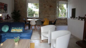 A living room with a blue sofa, white armchairs, a wooden coffee table, and a dining area with a table and chairs. - Country house with private heated pool 15mn from the sea (Vendres)